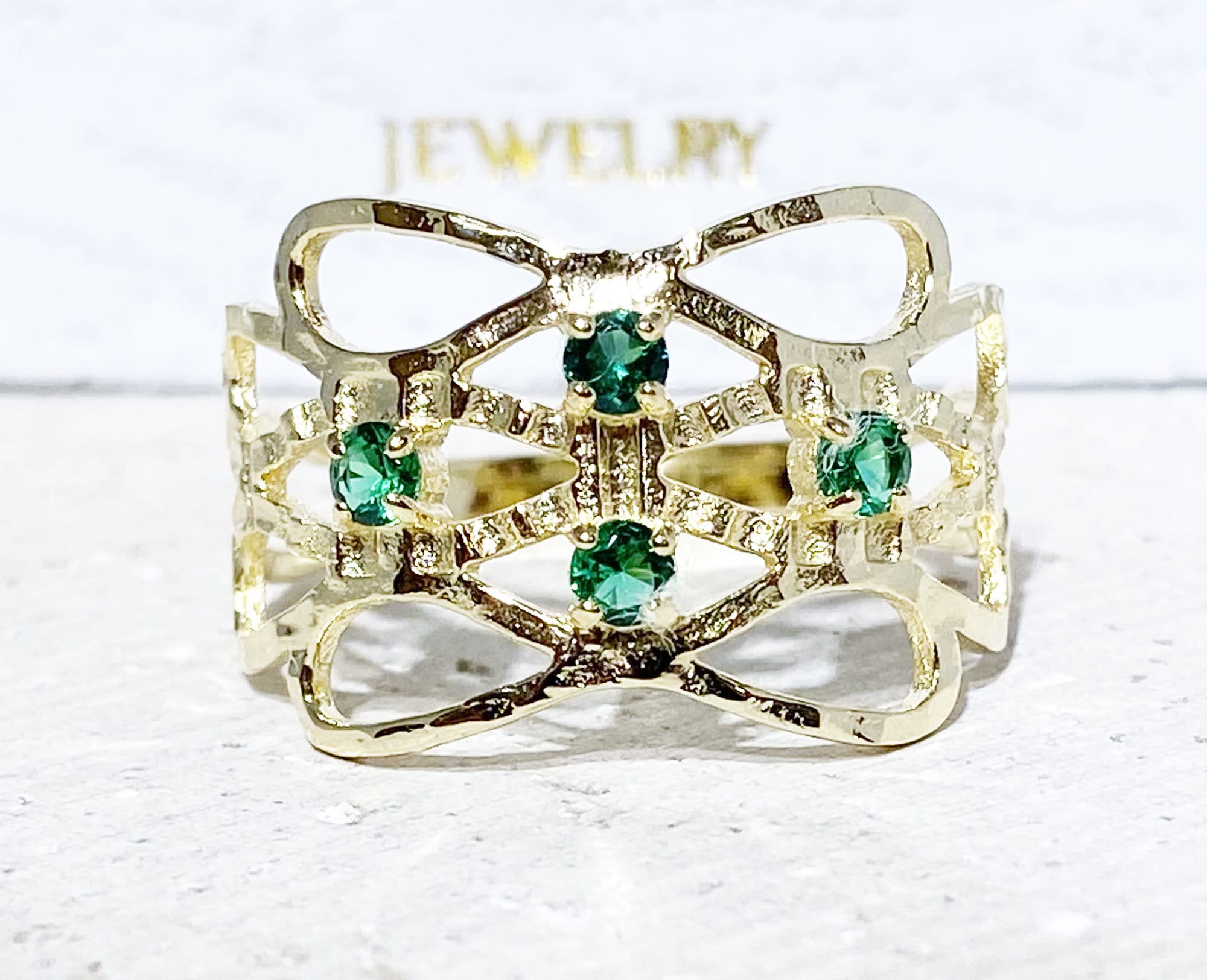 This gorgeous emerald ring displays simple elegance in its design. The ring features a round-cut emerald gemstones and finished with a hammered band.