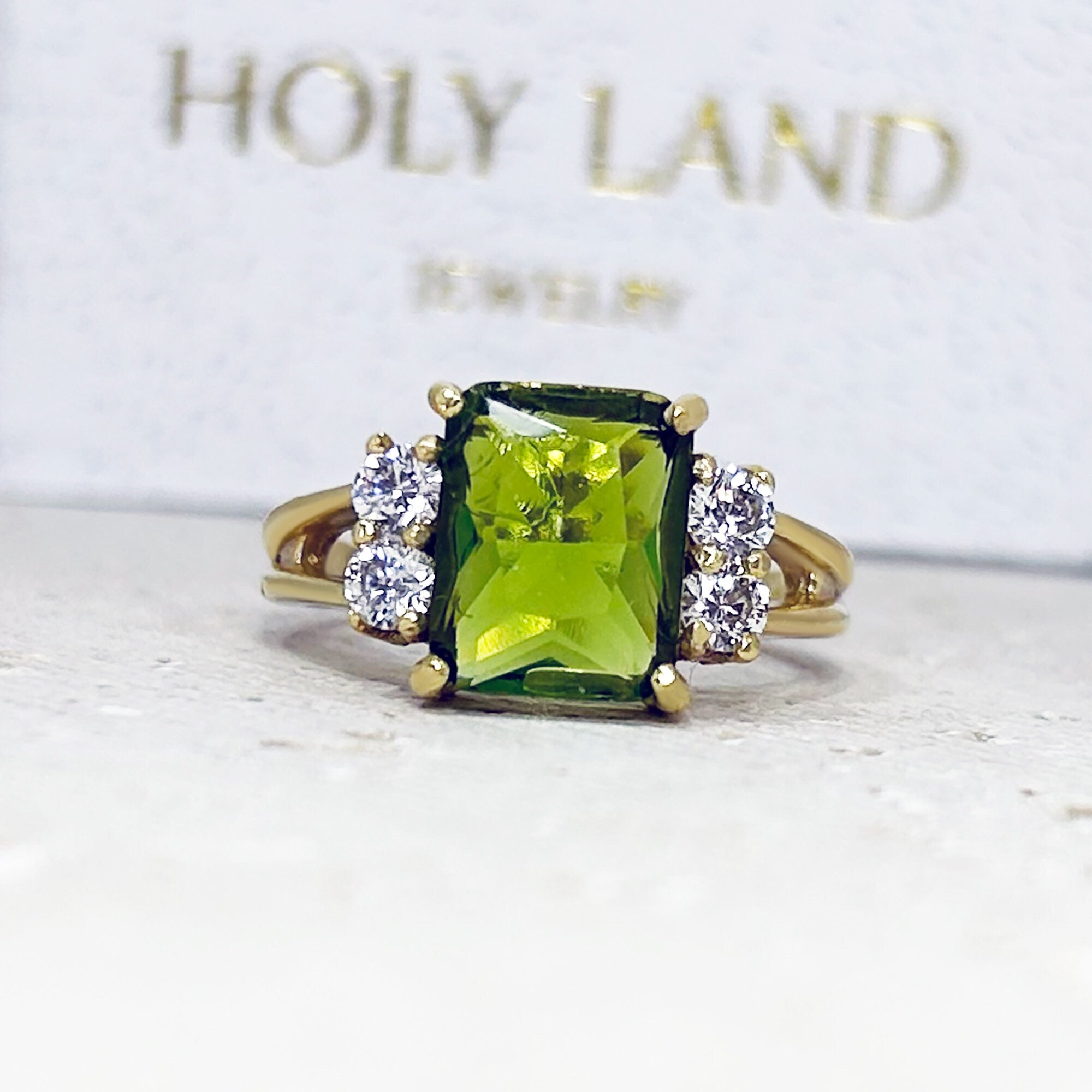 An absolute stunner, classic peridot engagement ring with an emerald cut gemstone of your choice as it’s centre stone and with round cut clear quartz on the band to further accentuate it.