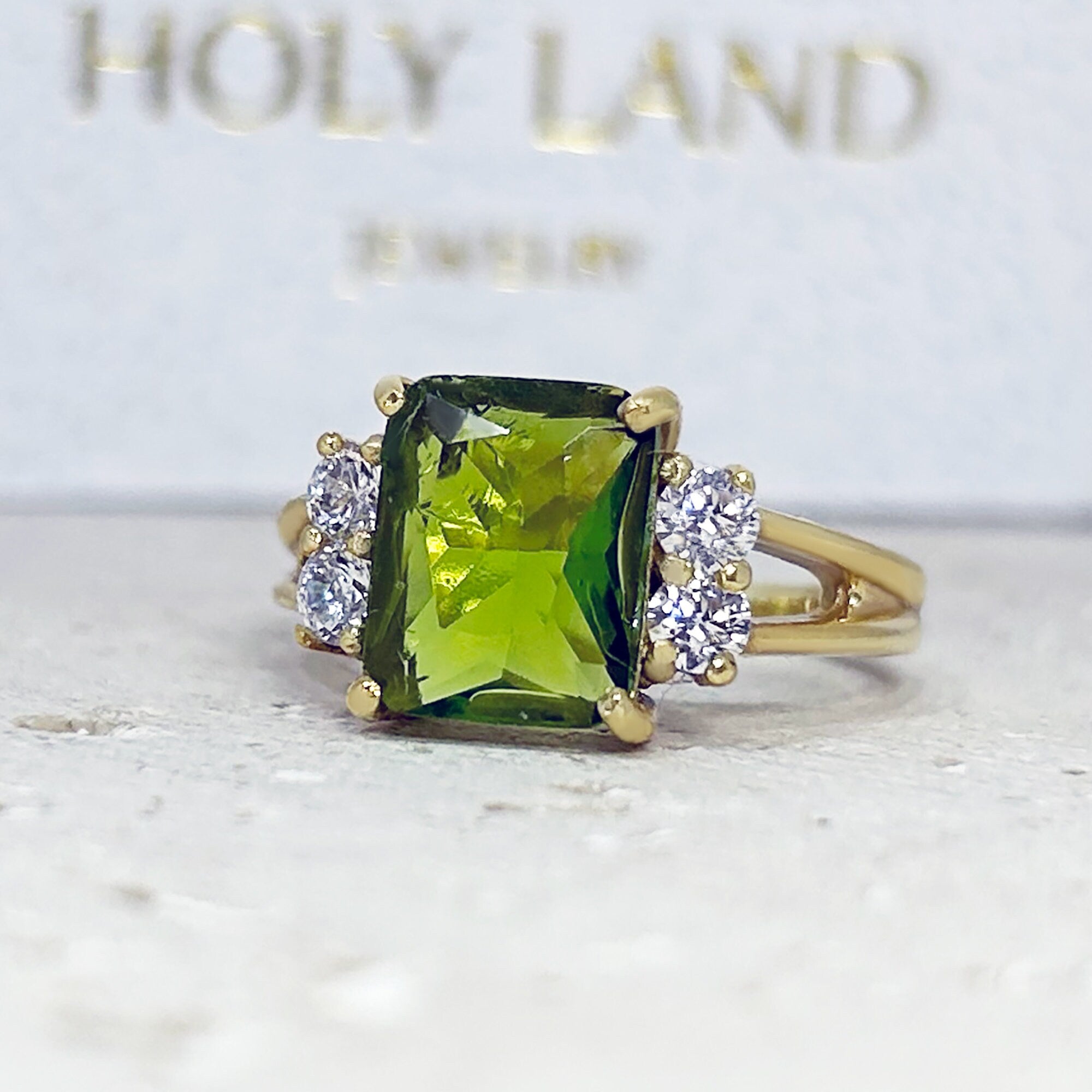 An absolute stunner, classic peridot engagement ring with an emerald cut gemstone of your choice as it’s centre stone and with round cut clear quartz on the band to further accentuate it.