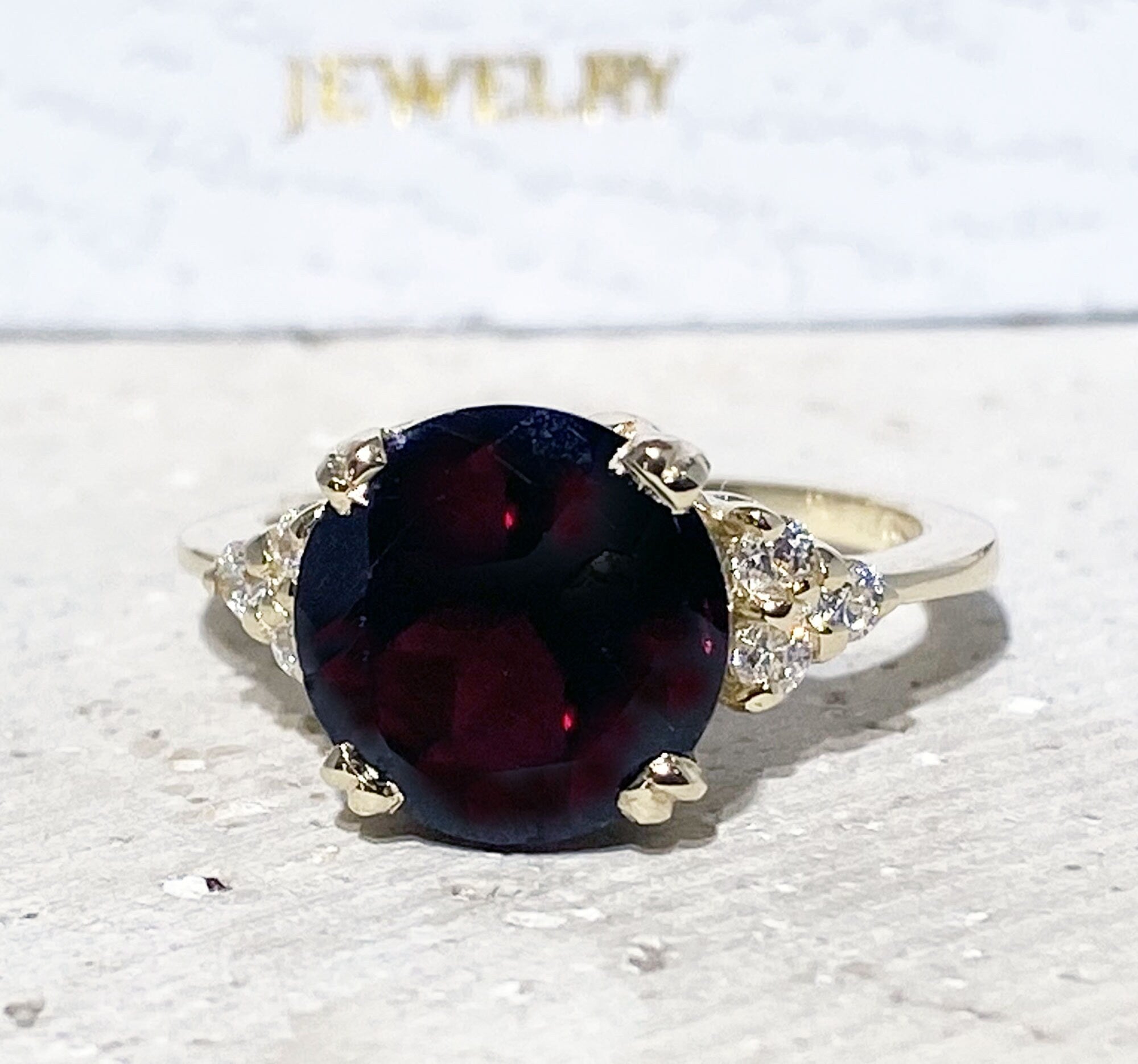 An absolute stunner, classic natural red garnet engagement ring with a round cut gemstone of your choice as it’s centre stone and with round cut clear quartz on the band to further accentuate it.