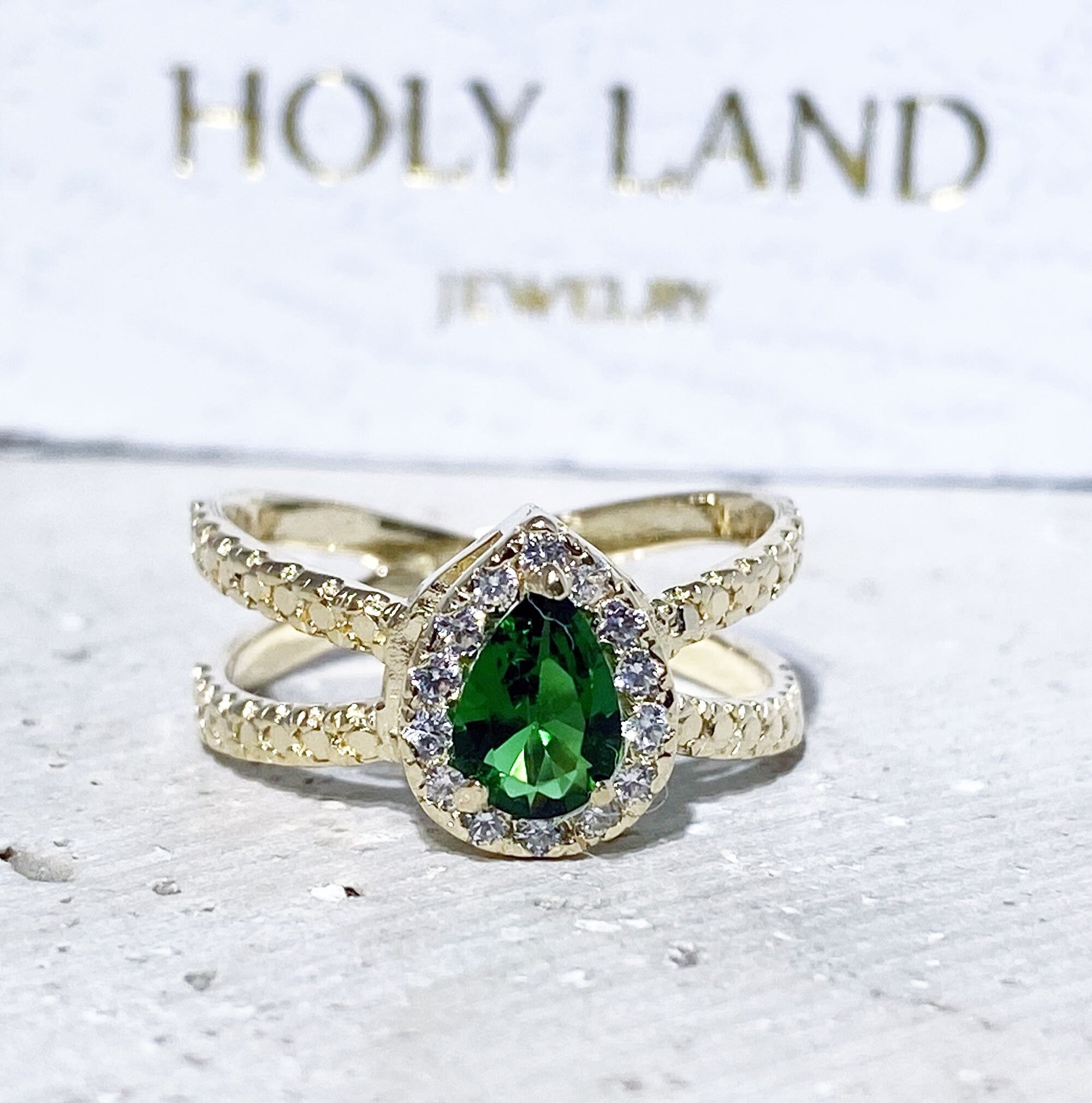 The spectacular design of this emerald ring is a contemporary take on a classic choice which will be much loved by anyone who loves bright and bold jewelry. The pear cut emerald is flanked on every side by high quality clear quartz gemstones.