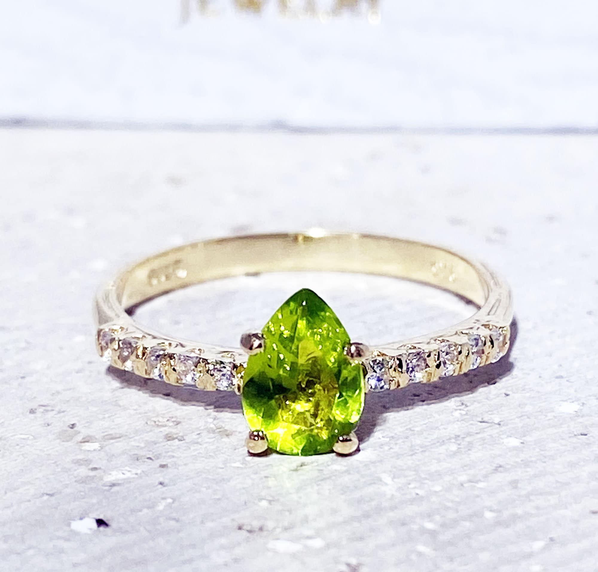 An absolute stunner, classic natural peridot engagement ring with a pear cut gemstone of your choice as it’s centre stone and with round cut clear quartz on the band to further accentuate it.