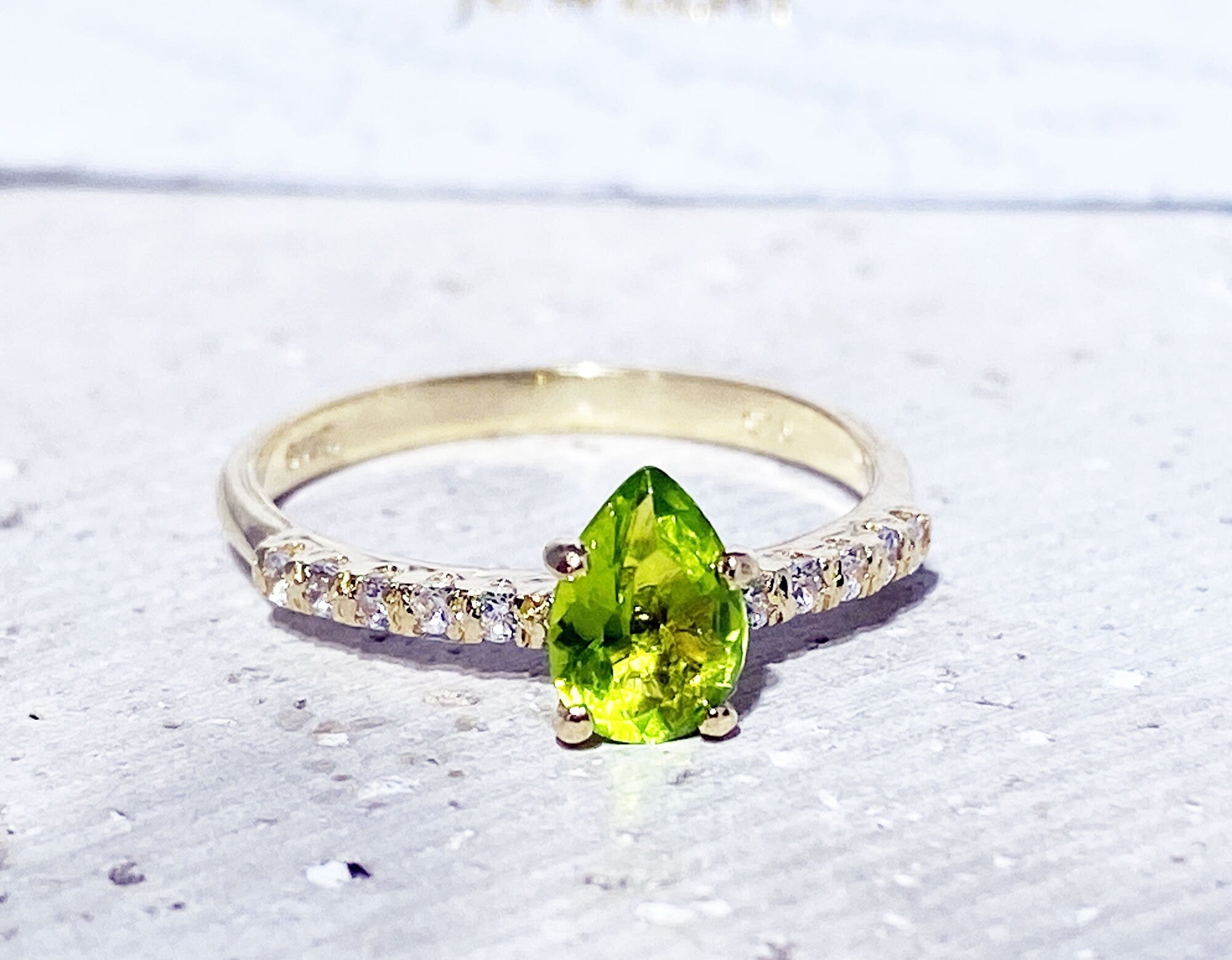 An absolute stunner, classic natural peridot engagement ring with a pear cut gemstone of your choice as it’s centre stone and with round cut clear quartz on the band to further accentuate it.