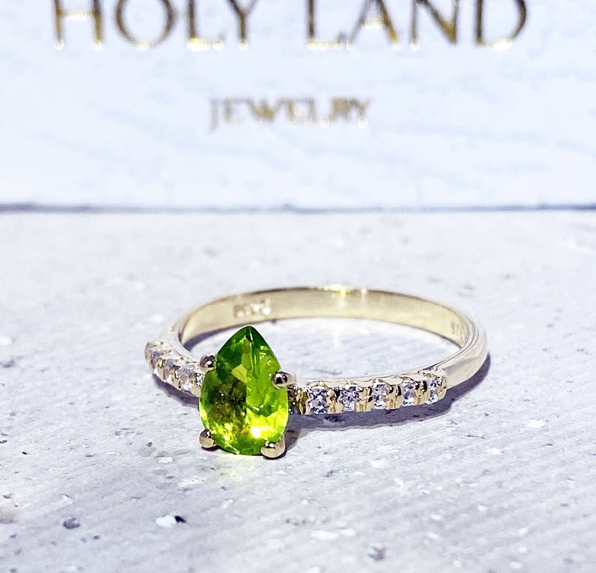 An absolute stunner, classic natural peridot engagement ring with a pear cut gemstone of your choice as it’s centre stone and with round cut clear quartz on the band to further accentuate it.