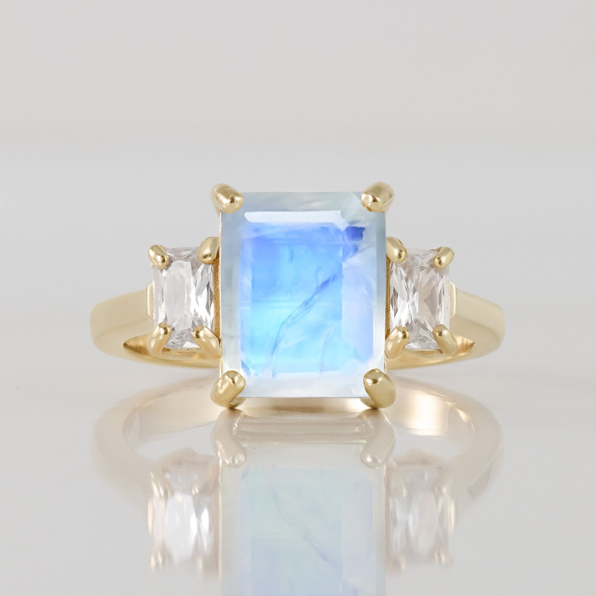 An absolute stunner, classic natural rainbow moonstone engagement ring with an emerald cut gemstone of your choice as it’s centre stone and with clear quartz on the band to further accentuate it.