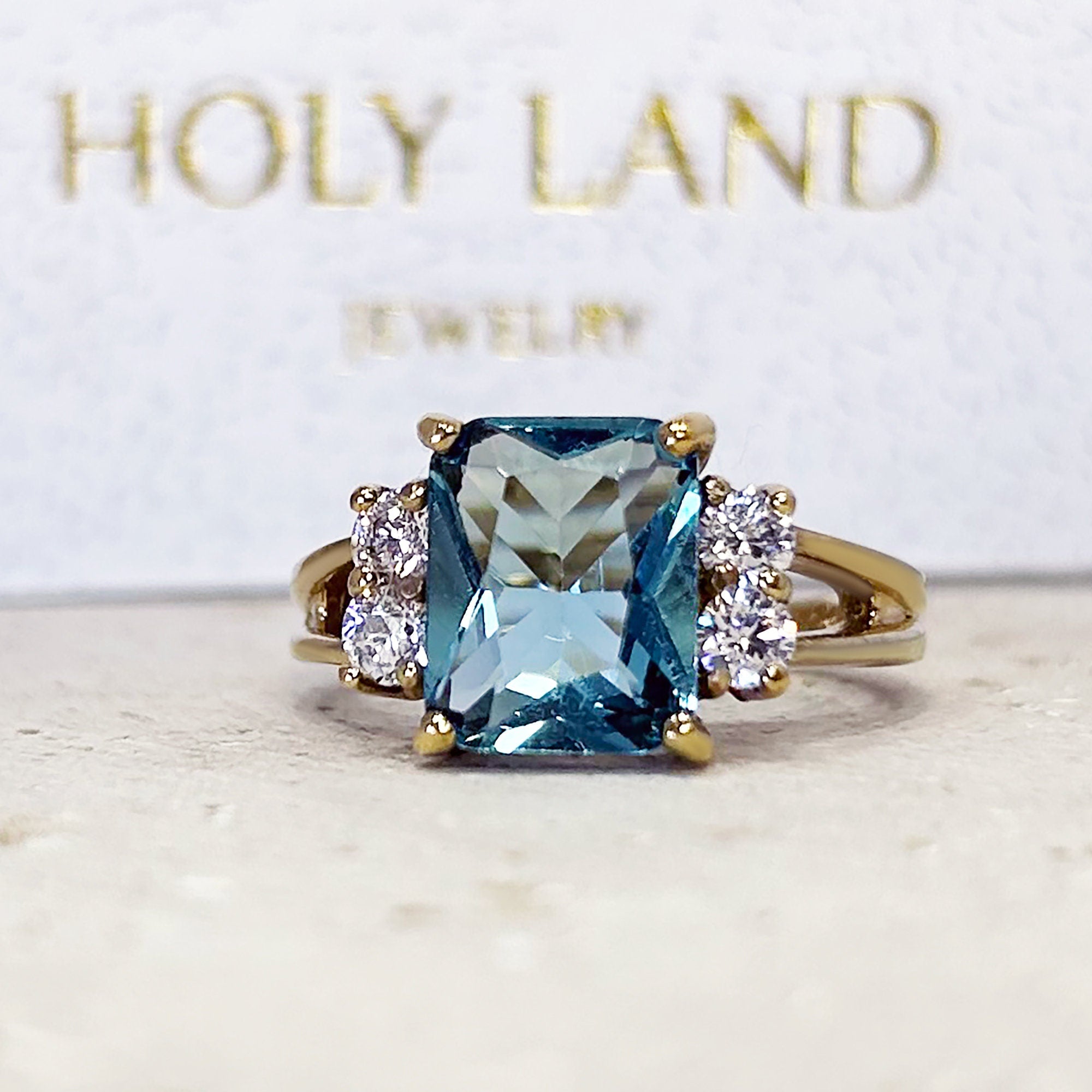 An absolute stunner, classic blue topaz engagement ring with an emerald cut gemstone of your choice as it’s centre stone and with round cut clear quartz on the band to further accentuate it.